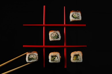 Photo of Tic-tac-toe game made with delicious sushi rolls and chopsticks on black background, flat lay