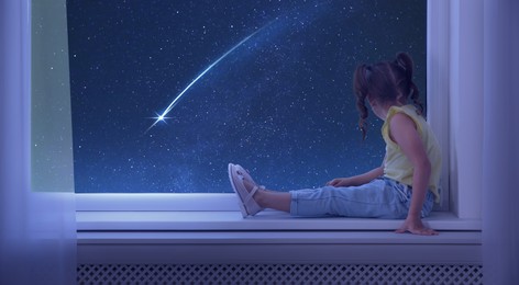 Image of Cute little girl sitting on windowsill and looking at shooting star in beautiful night sky
