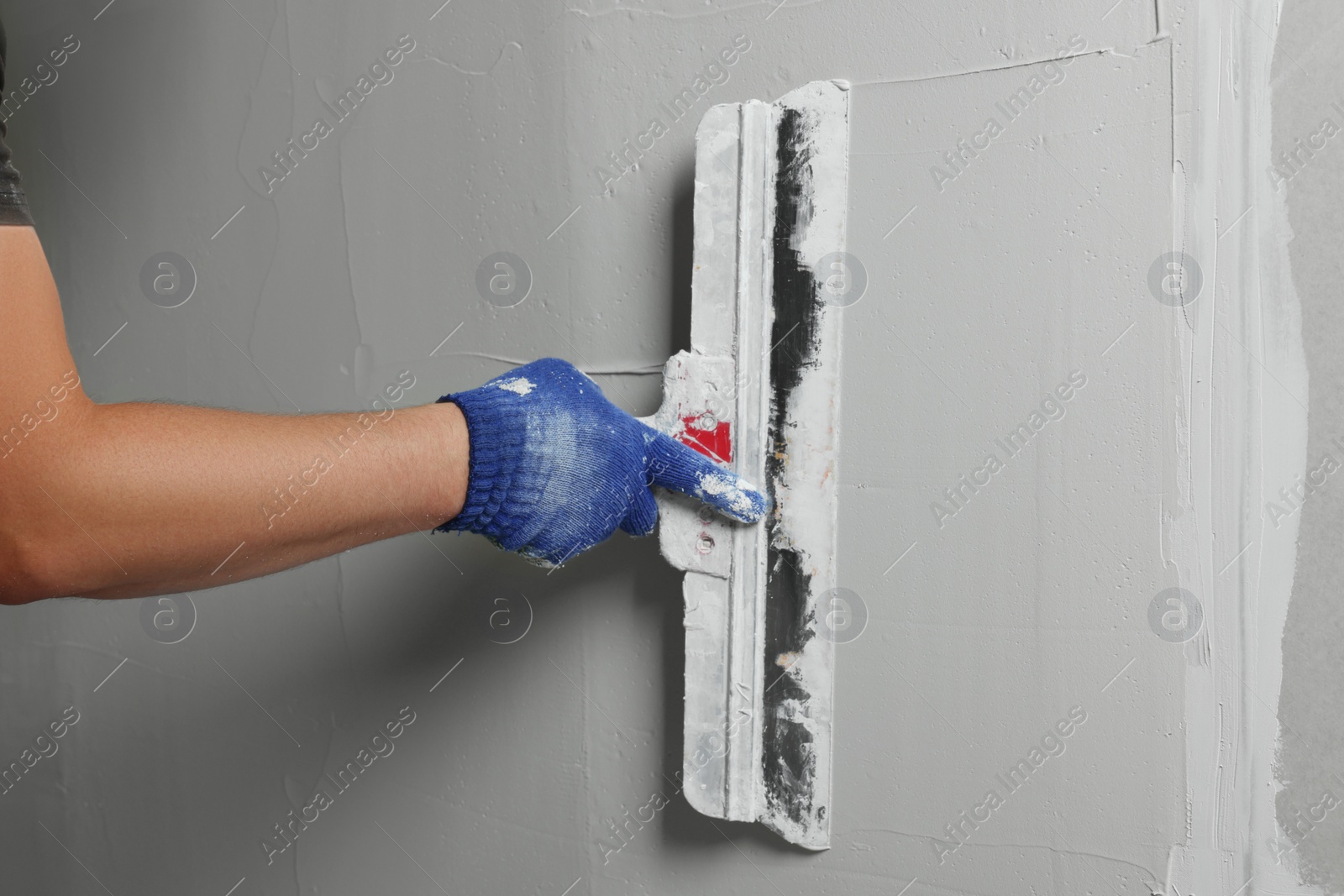 Photo of Professional worker plastering wall with putty knife, closeup