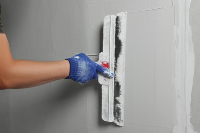 Photo of Professional worker plastering wall with putty knife, closeup