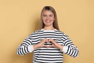 Photo of Happy volunteer making heart with her hands on beige background