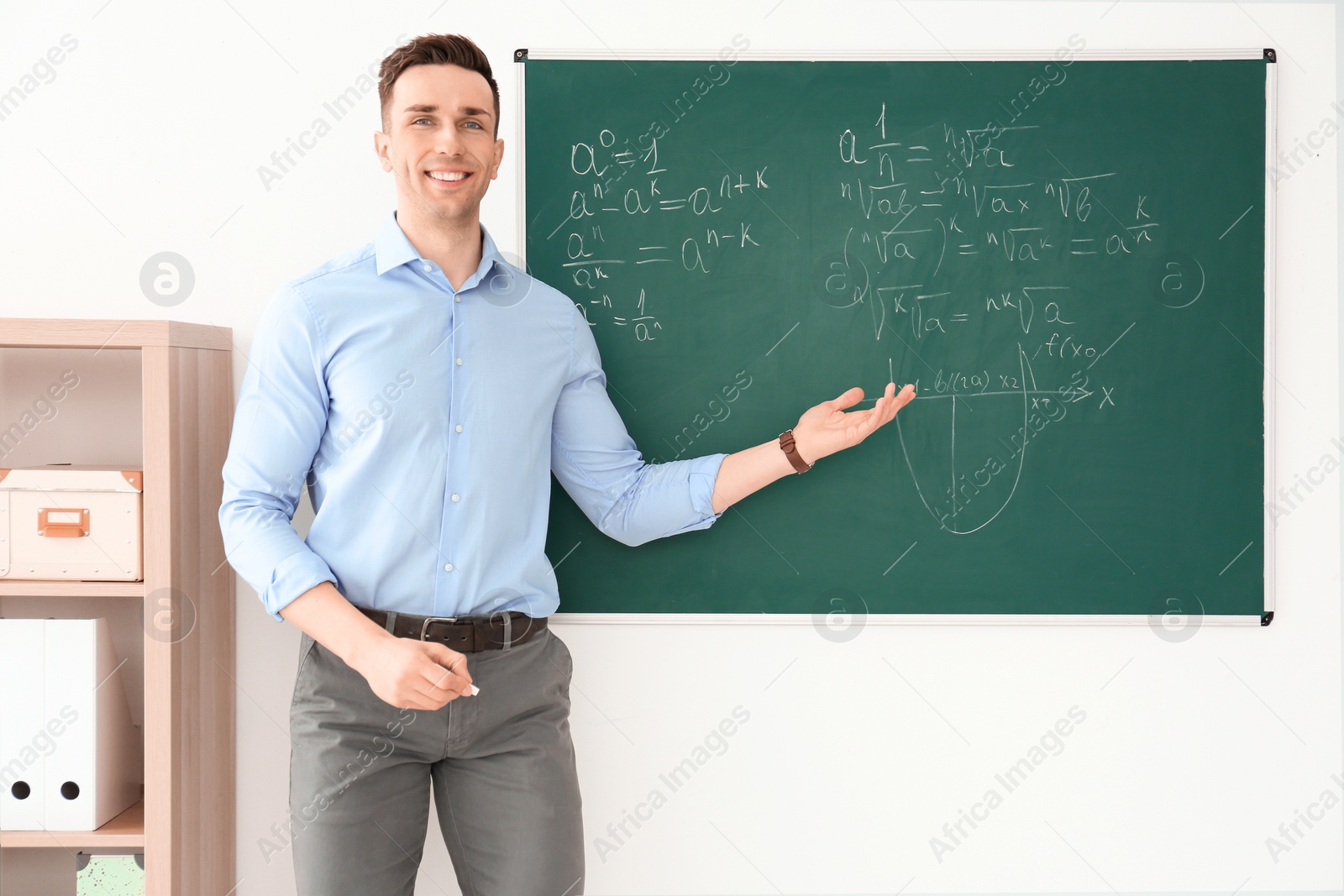 Photo of Young male teacher explaining math formulas written on blackboard in classroom