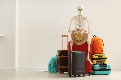 Photo of Waiting concept. Human skeleton with hat and suitcases indoors, space for text