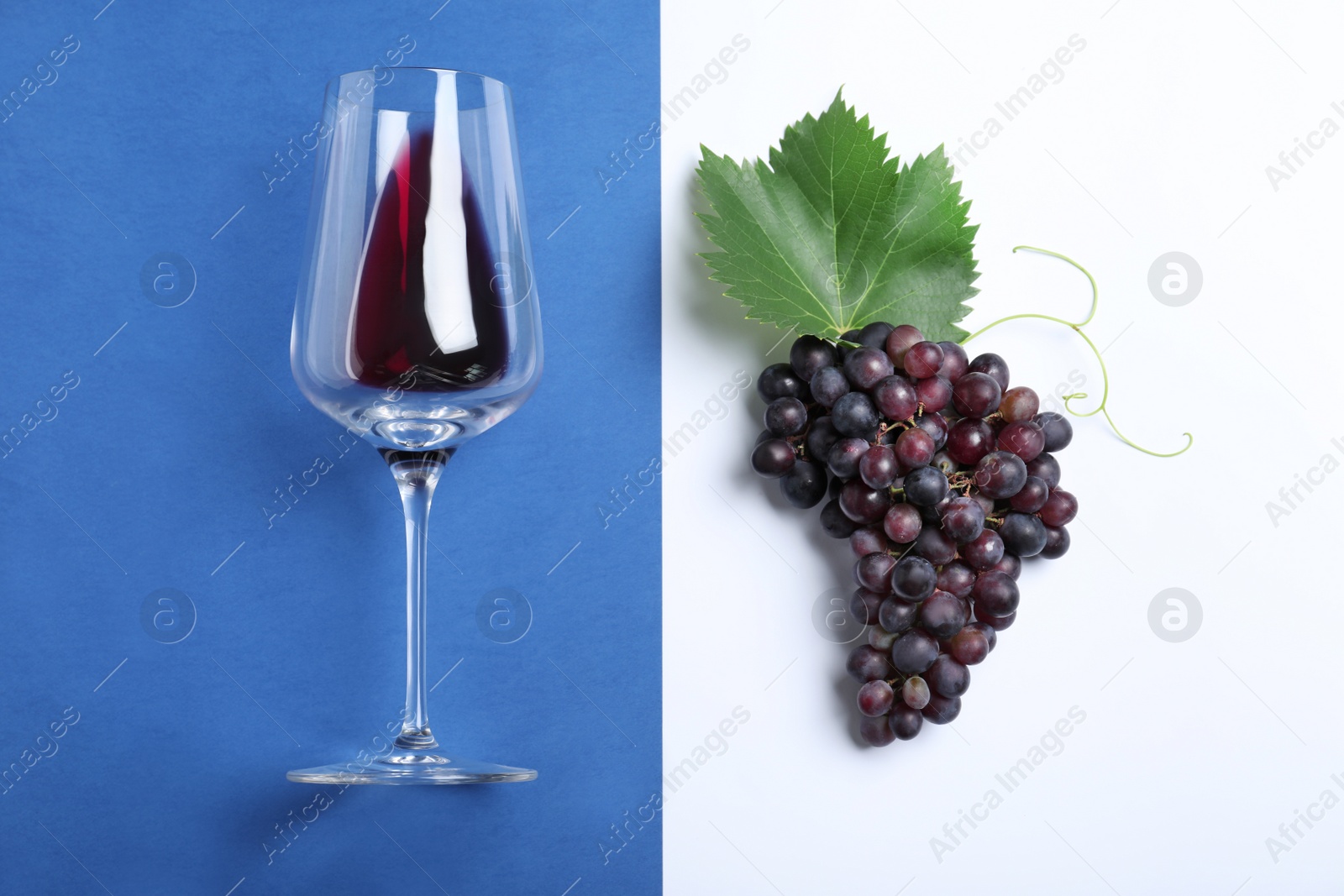 Photo of Fresh ripe juicy grapes and glass of wine on color background, flat lay