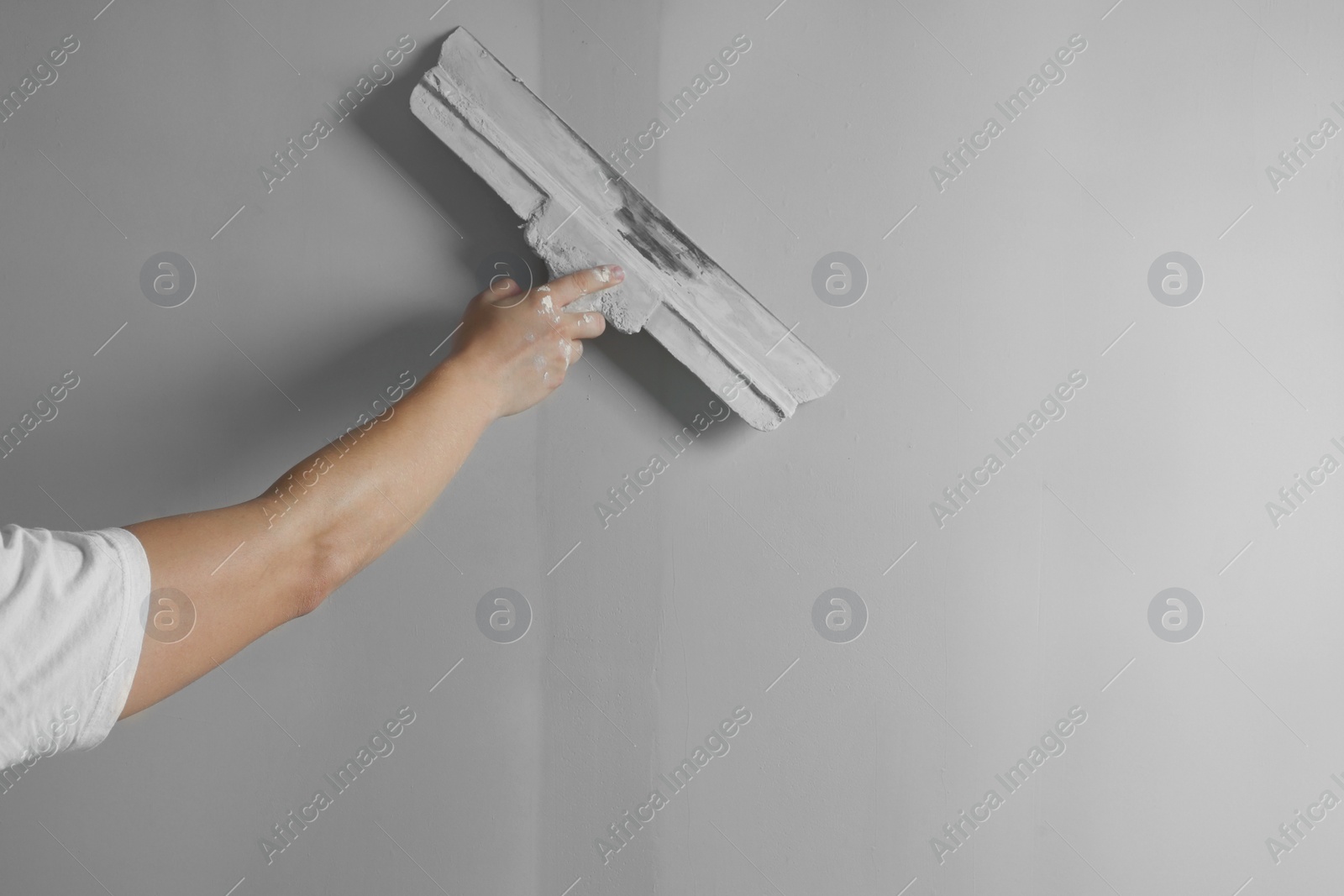 Photo of Professional worker plastering wall with putty knife, closeup