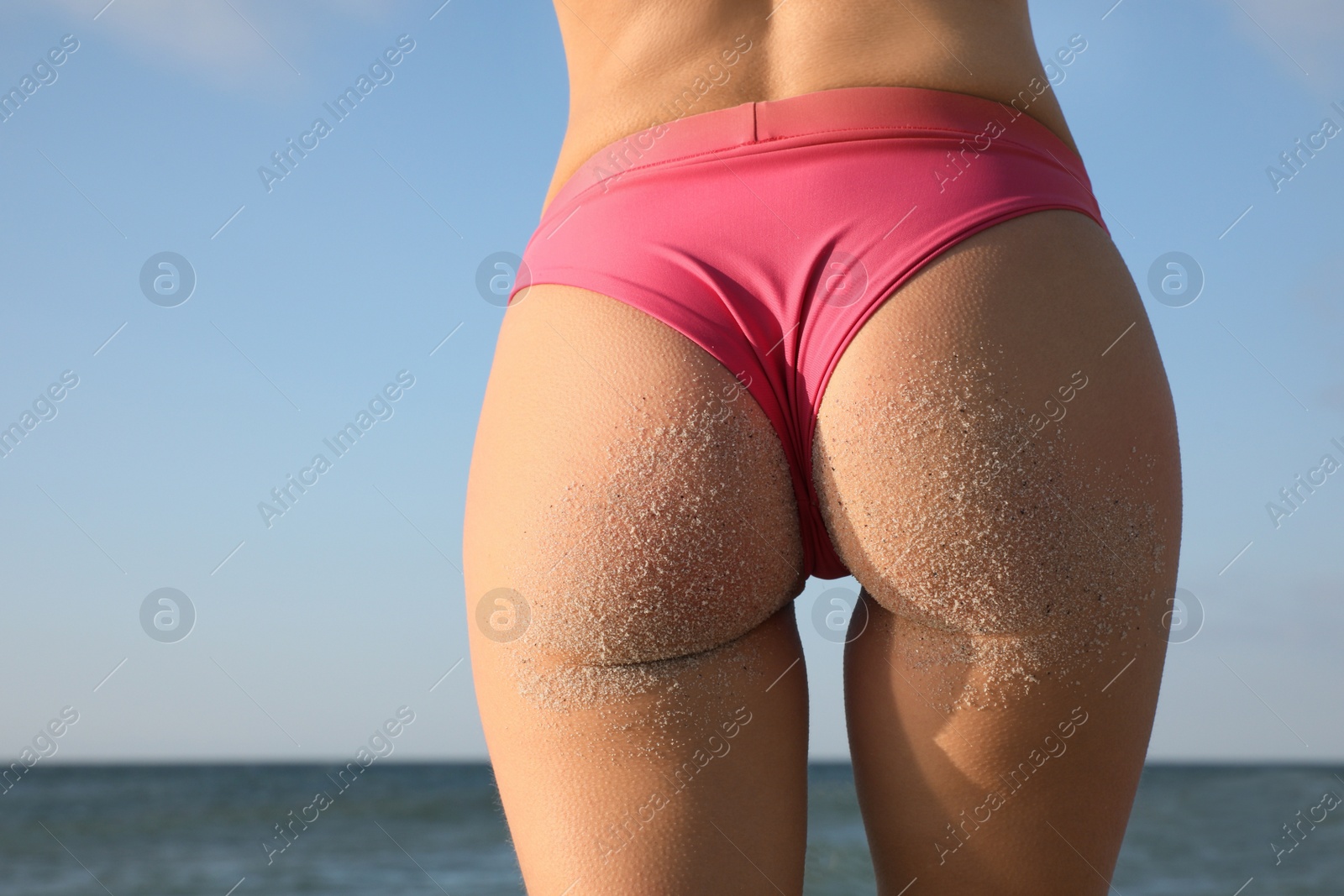 Photo of Woman with sand on beautiful body in bikini near sea, closeup. Back view