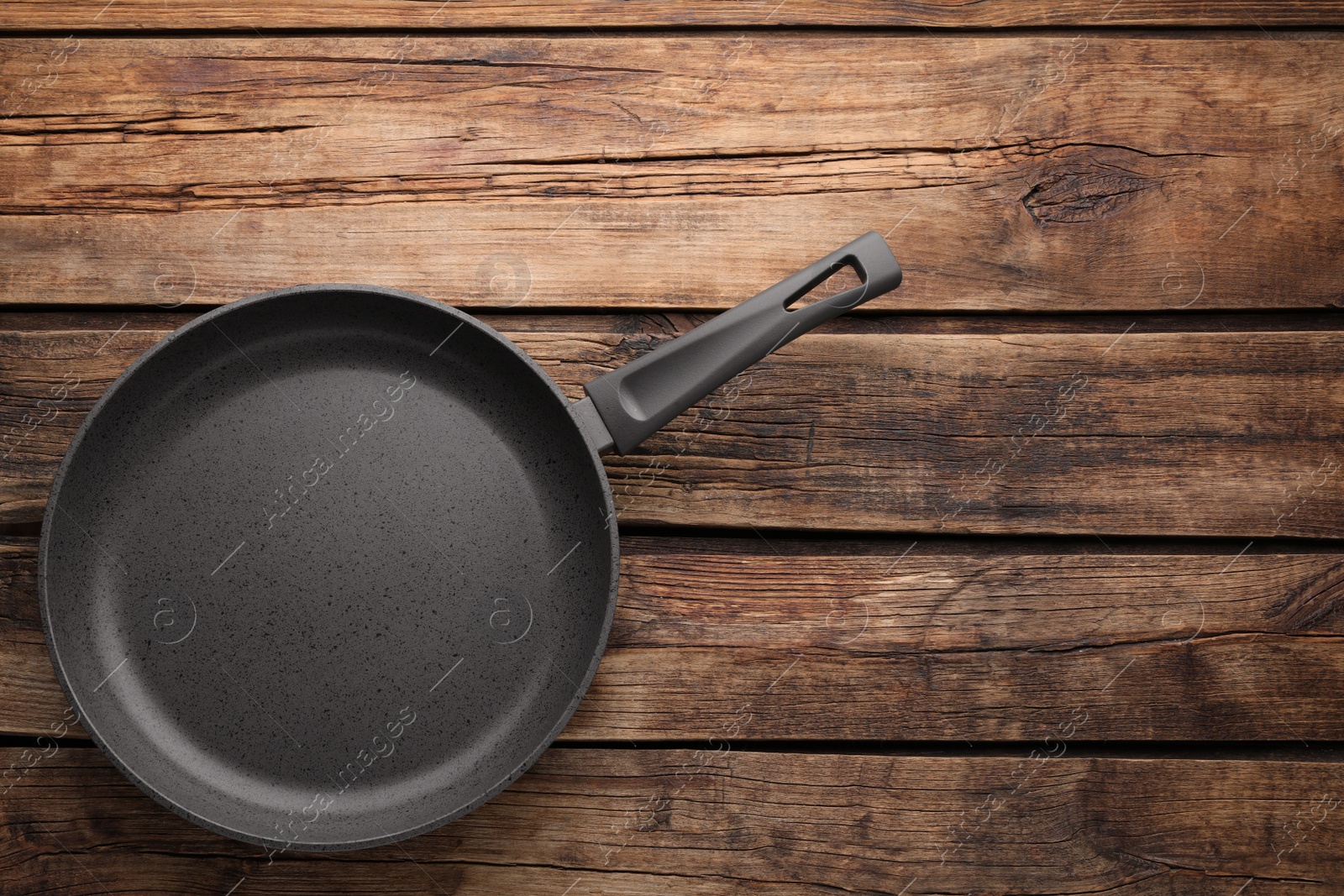 Photo of New non-stick frying pan on wooden table, top view. Space for text