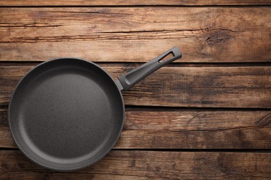 Photo of New non-stick frying pan on wooden table, top view. Space for text
