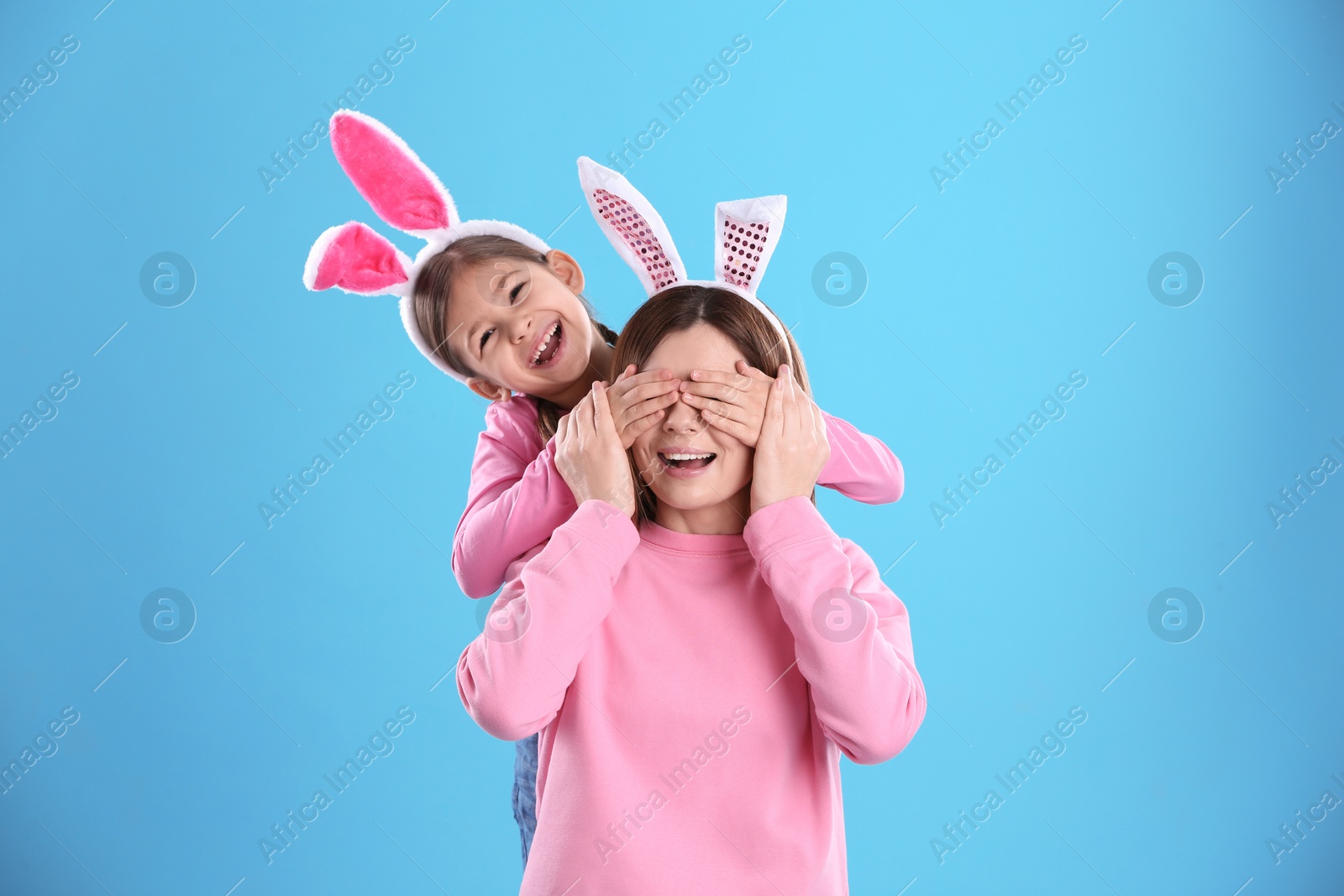 Photo of Happy woman and daughter with bunny ears on color background
