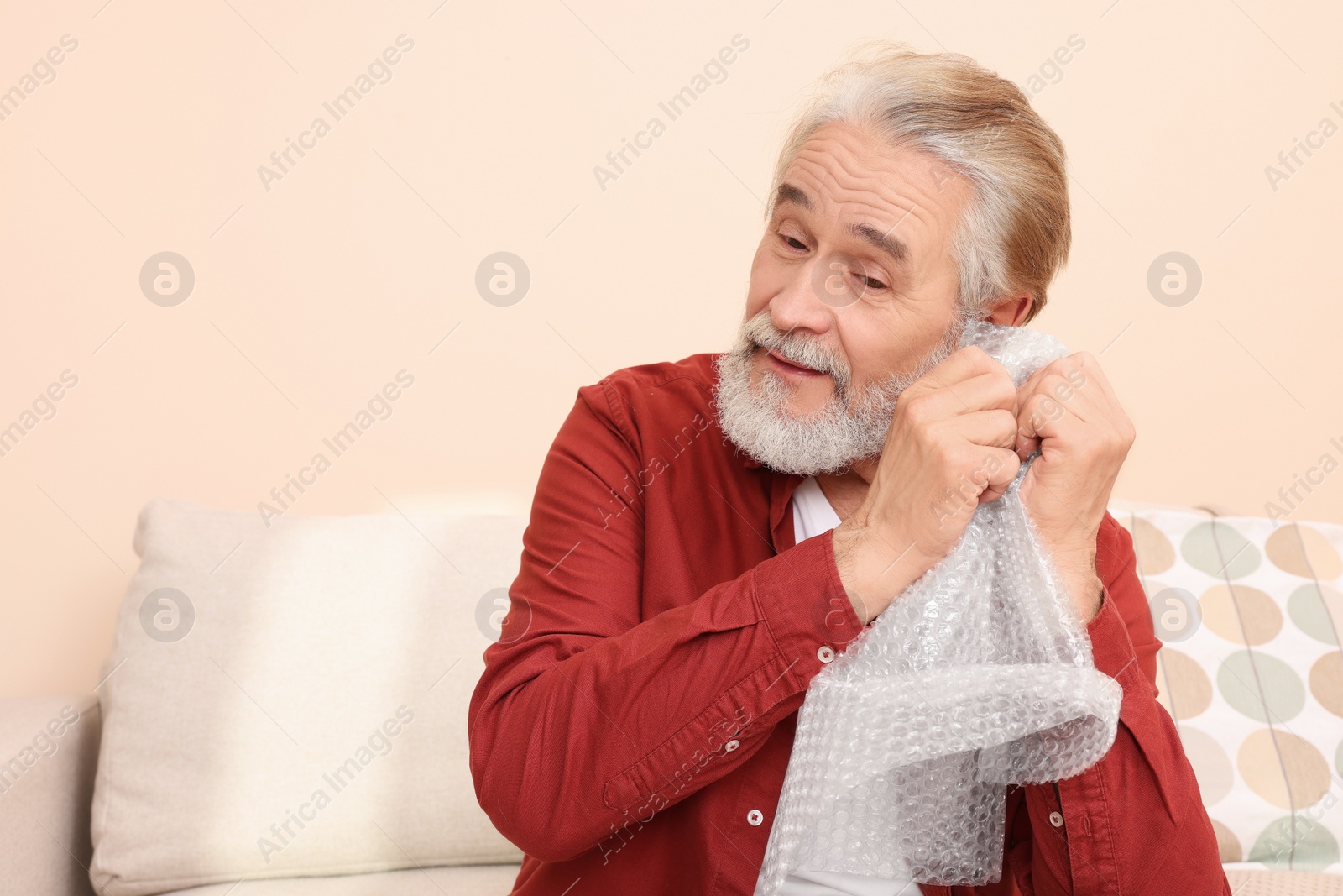 Photo of Senior man popping bubble wrap at home, space for text. Stress relief