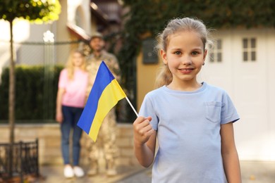 Child with Ukrainian flag, her father in military uniform and mother outdoors, space for text. Family reunion