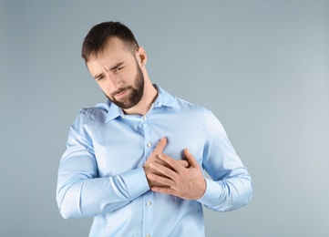 Young man suffering from chest pain on light background