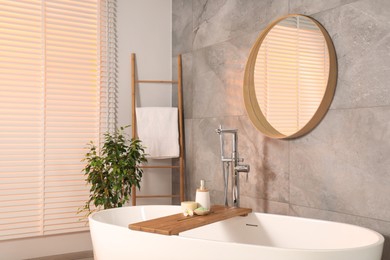 Stylish bathroom interior with ceramic tub, spa products and mirror