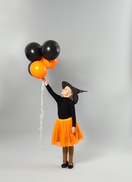 Photo of Cute little girl with balloons wearing Halloween costume on grey background