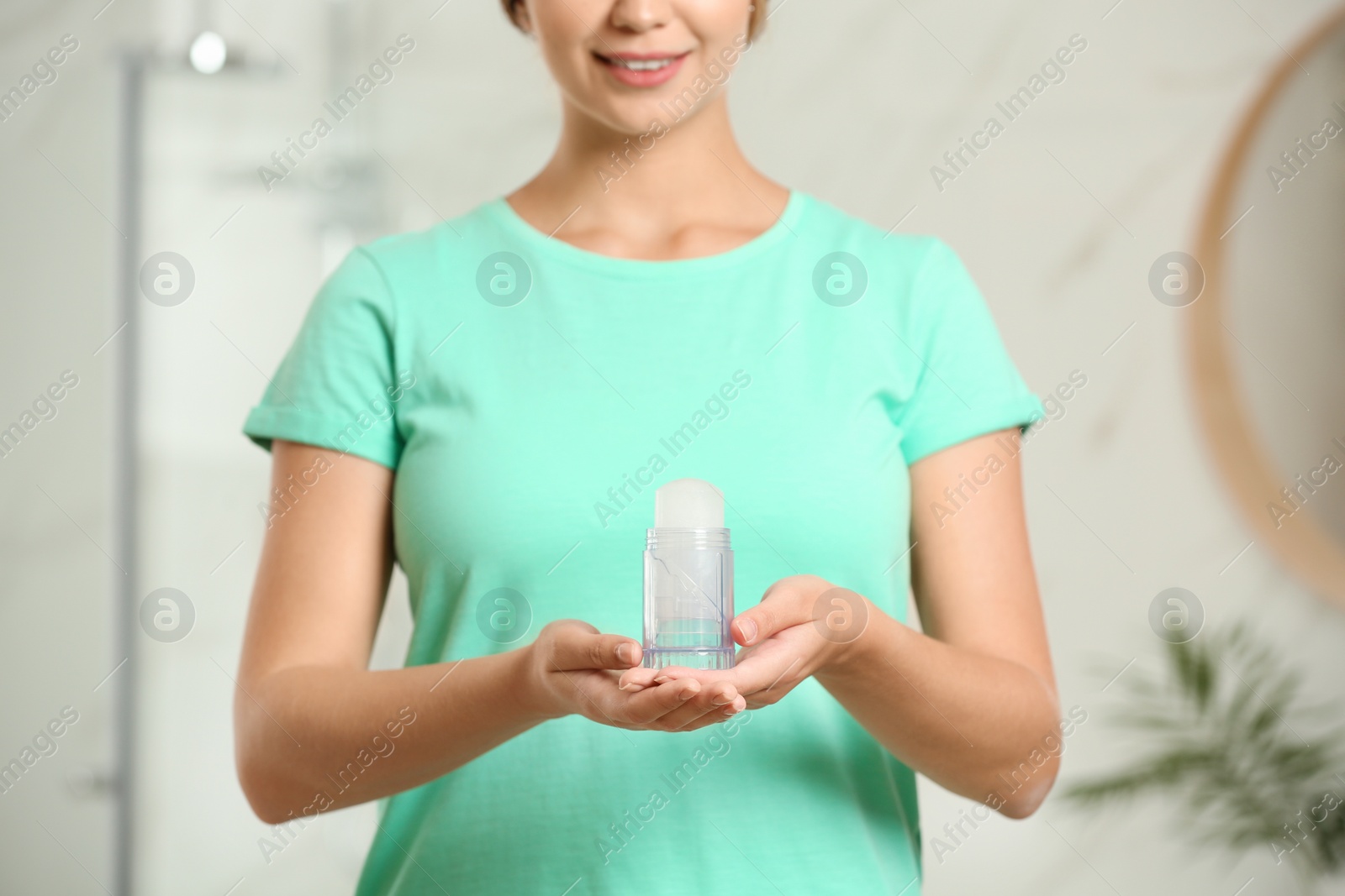 Photo of Young woman holding crystal alum deodorant indoors, closeup. Mockup for design