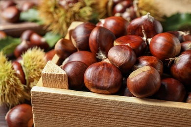 Fresh sweet edible chestnuts in wooden crate, closeup