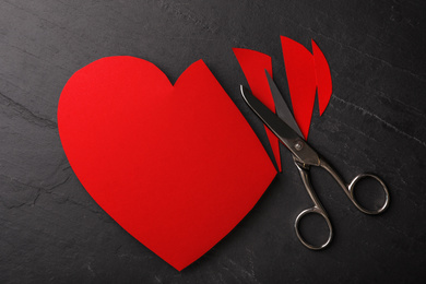 Cut paper heart and scissors on black stone background, flat lay. Relationship problems concept