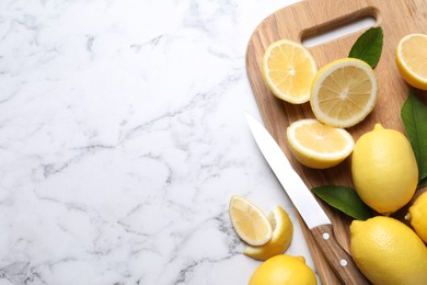 Photo of Many fresh ripe lemons with green leaves and knife on white marble table, flat lay. Space for text