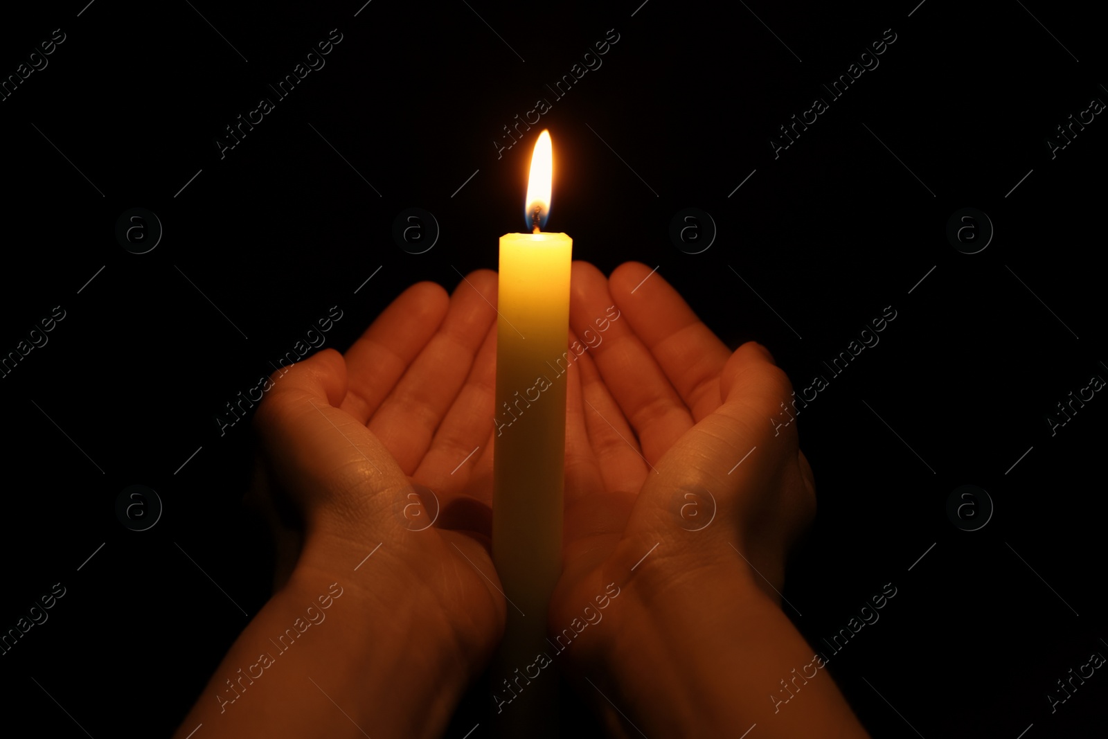 Photo of Woman holding burning candle in hands on black background, closeup