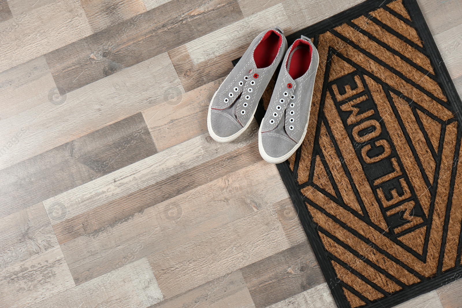 Photo of New clean doormat with word WELCOME and shoes on floor, top view. Space for text