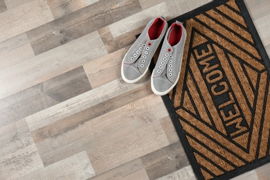 New clean doormat with word WELCOME and shoes on floor, top view. Space for text