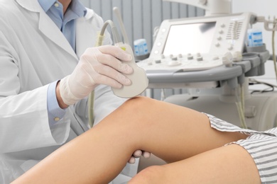 Doctor conducting ultrasound examination of patient's knee in clinic, closeup