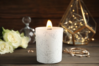 Photo of Burning candle and jewelry on wooden table
