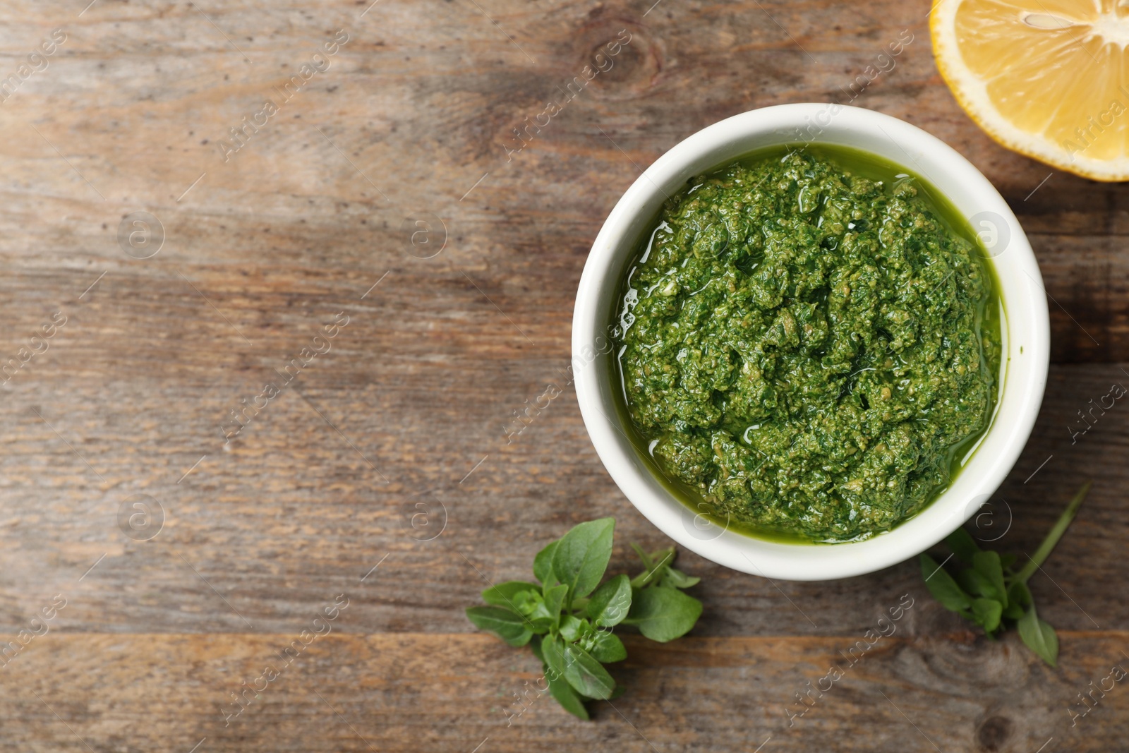 Photo of Homemade pesto sauce in bowl, basil leaves and lemon on table, top view with space for text