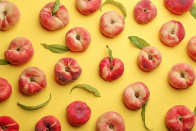 Photo of Fresh donut peaches with leaves on yellow background, flat lay
