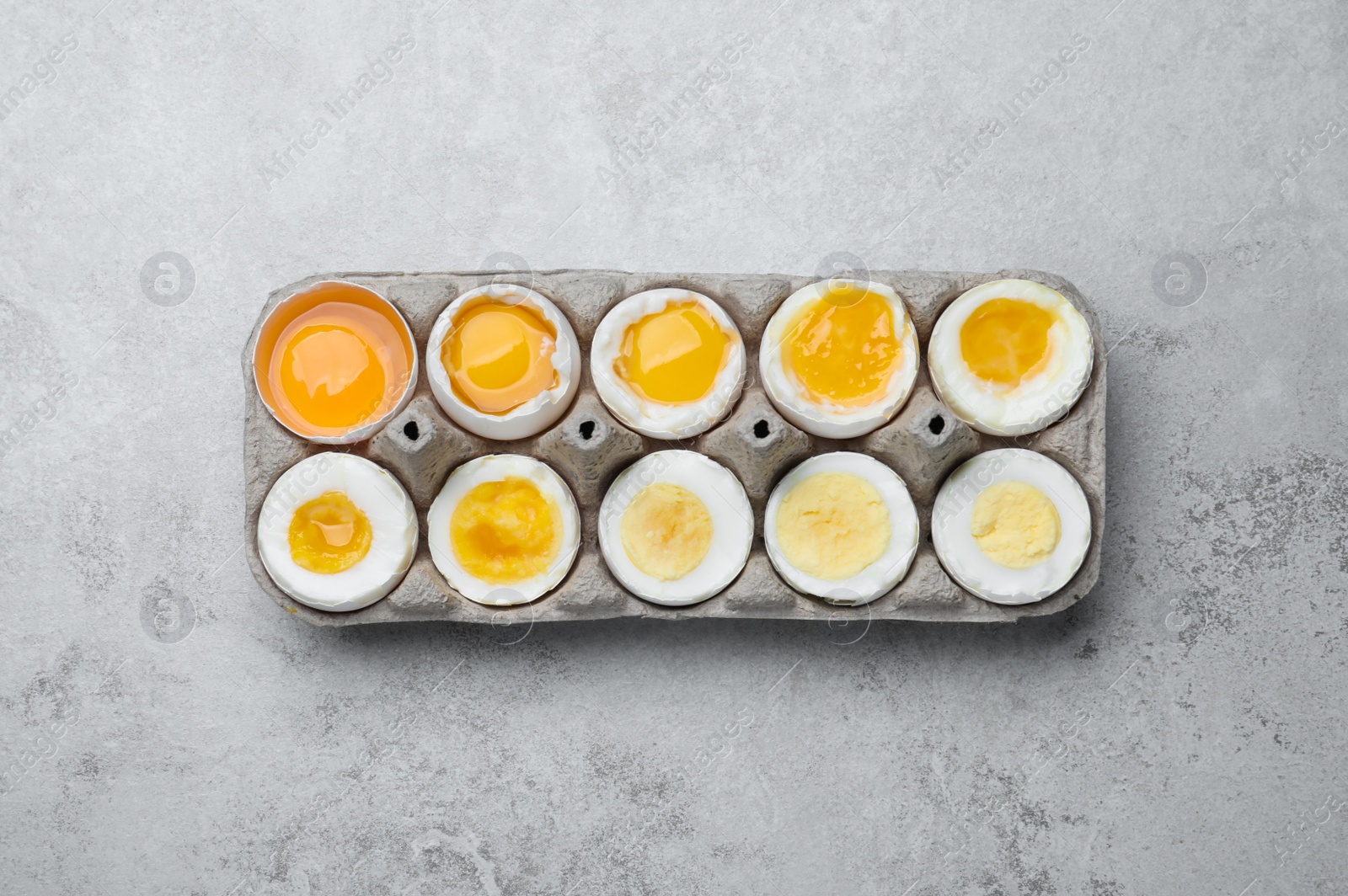 Photo of Boiled chicken eggs of different readiness stages in carton on light grey table, top view