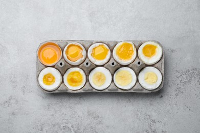 Photo of Boiled chicken eggs of different readiness stages in carton on light grey table, top view