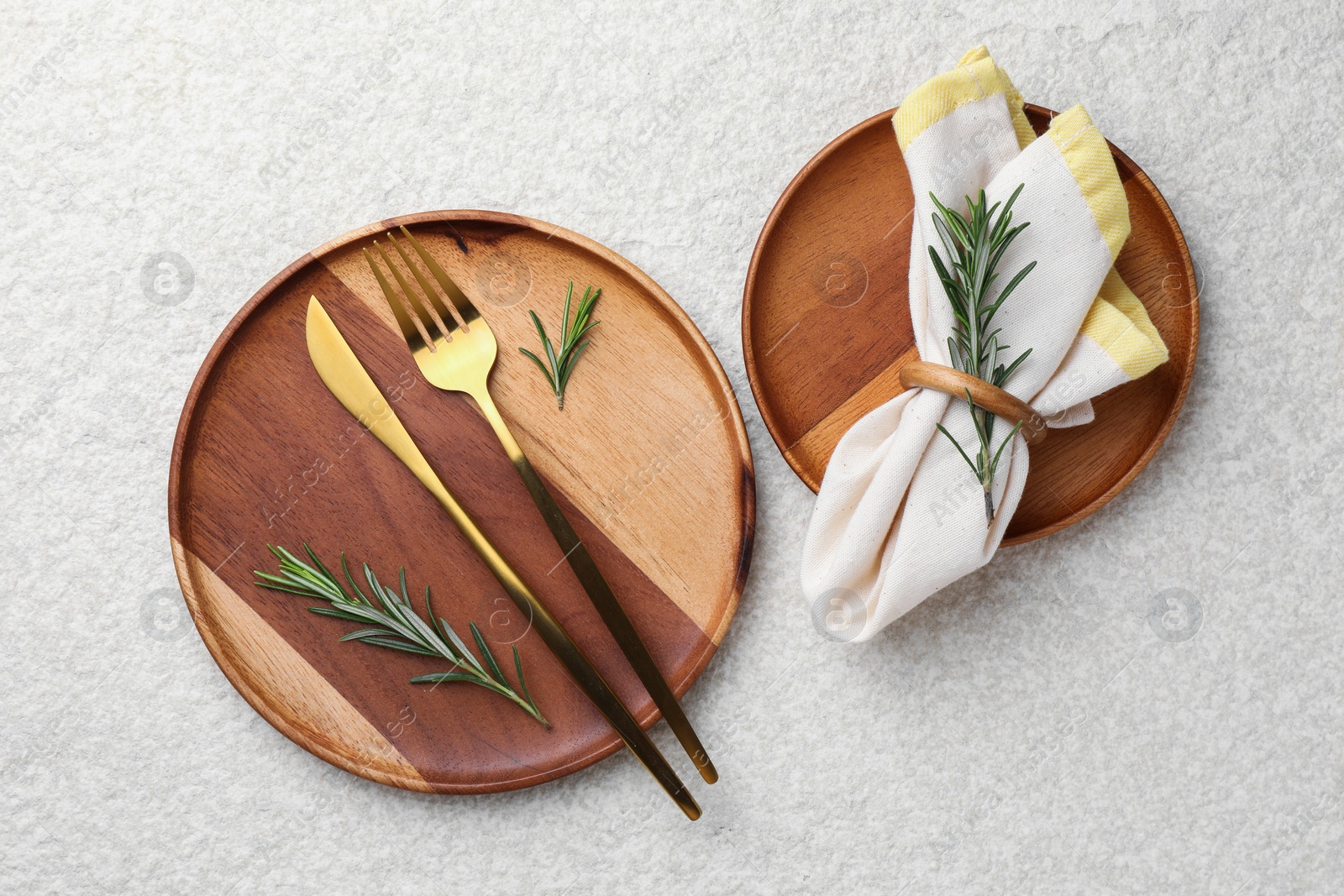 Photo of Stylish setting with cutlery, napkin, rosemary and plates on light textured table, flat lay