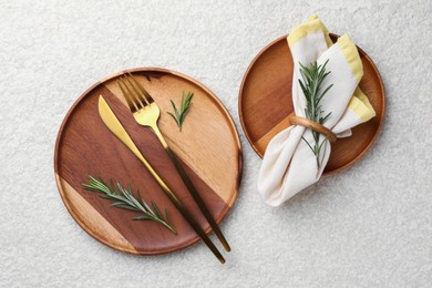 Stylish setting with cutlery, napkin, rosemary and plates on light textured table, flat lay