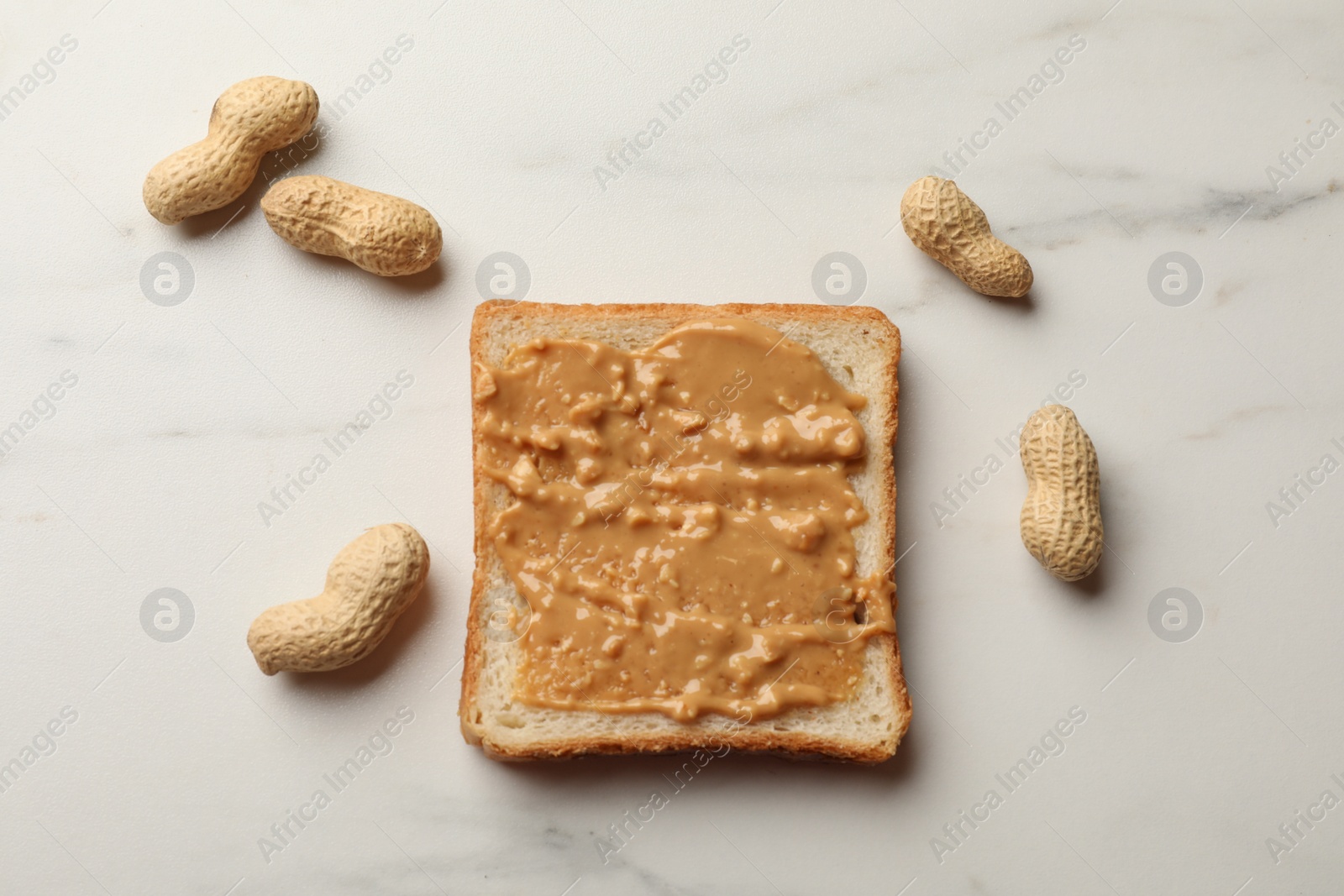 Photo of Delicious toast with peanut butter and nuts on white marble table, flat lay