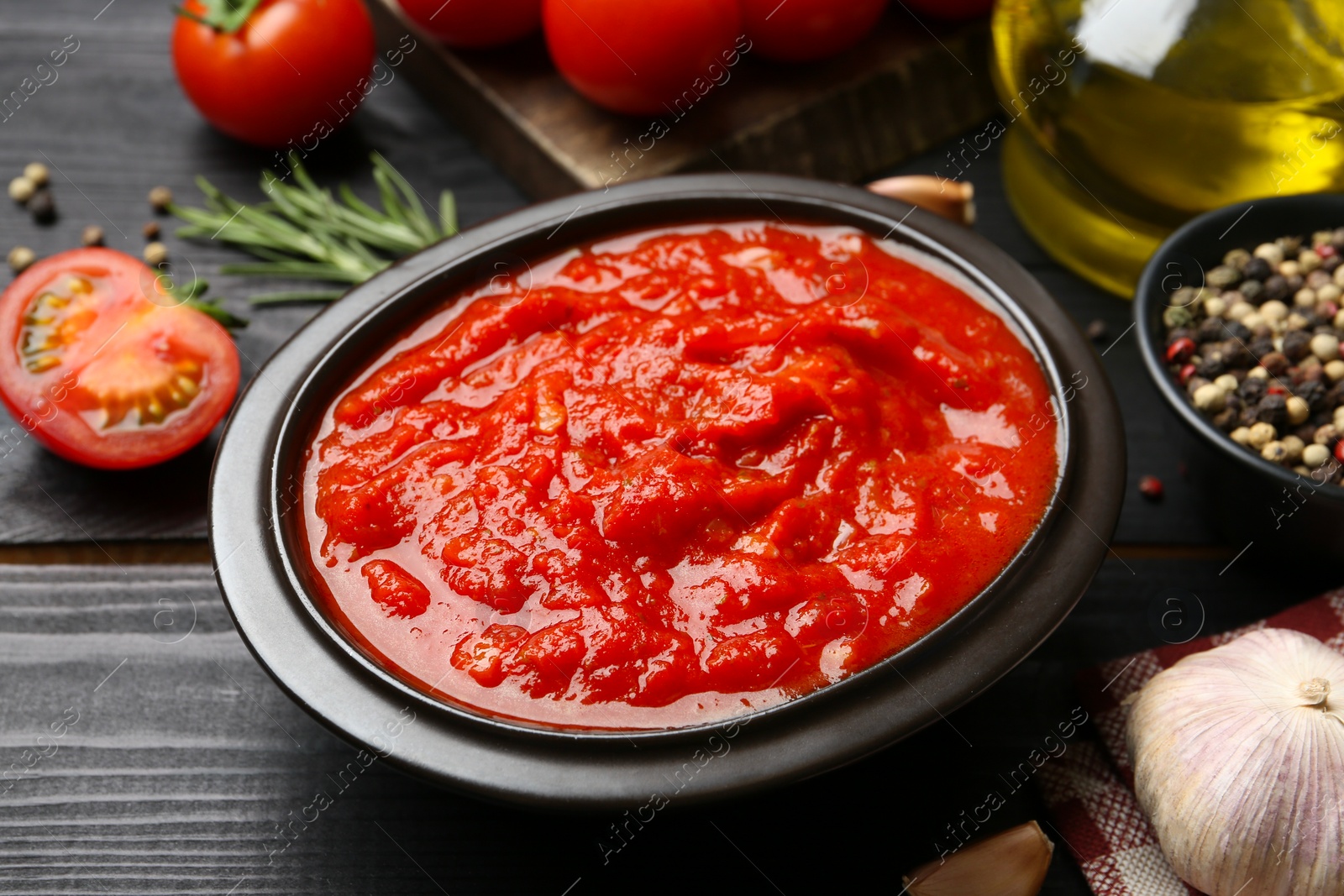 Photo of Homemade tomato sauce in bowl on black wooden table, closeup