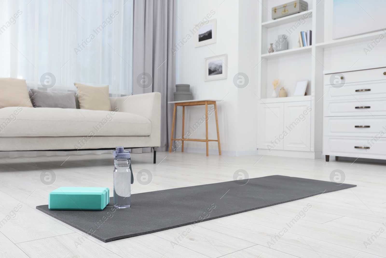 Photo of Exercise mat, yoga block and bottle of water on floor in room