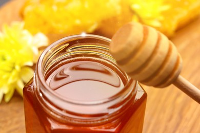 Natural honey in glass jar and wooden dipper under sunlight, closeup