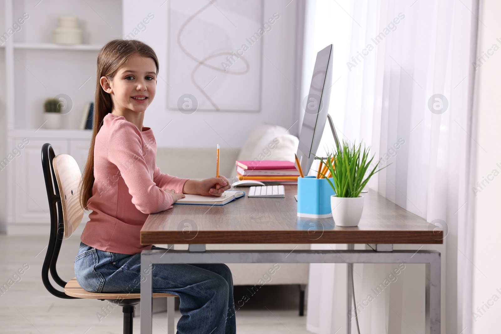 Photo of E-learning. Cute girl taking notes during online lesson at table indoors