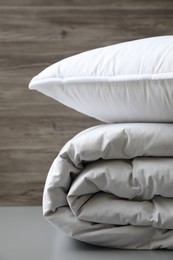 Photo of Soft folded blanket and pillow on light grey table, closeup