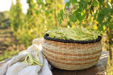 Photo of Wicker basket with fresh green beans on wooden table in garden