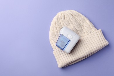 Fabric shaver with knitted hat on lilac background, top view. Space for text