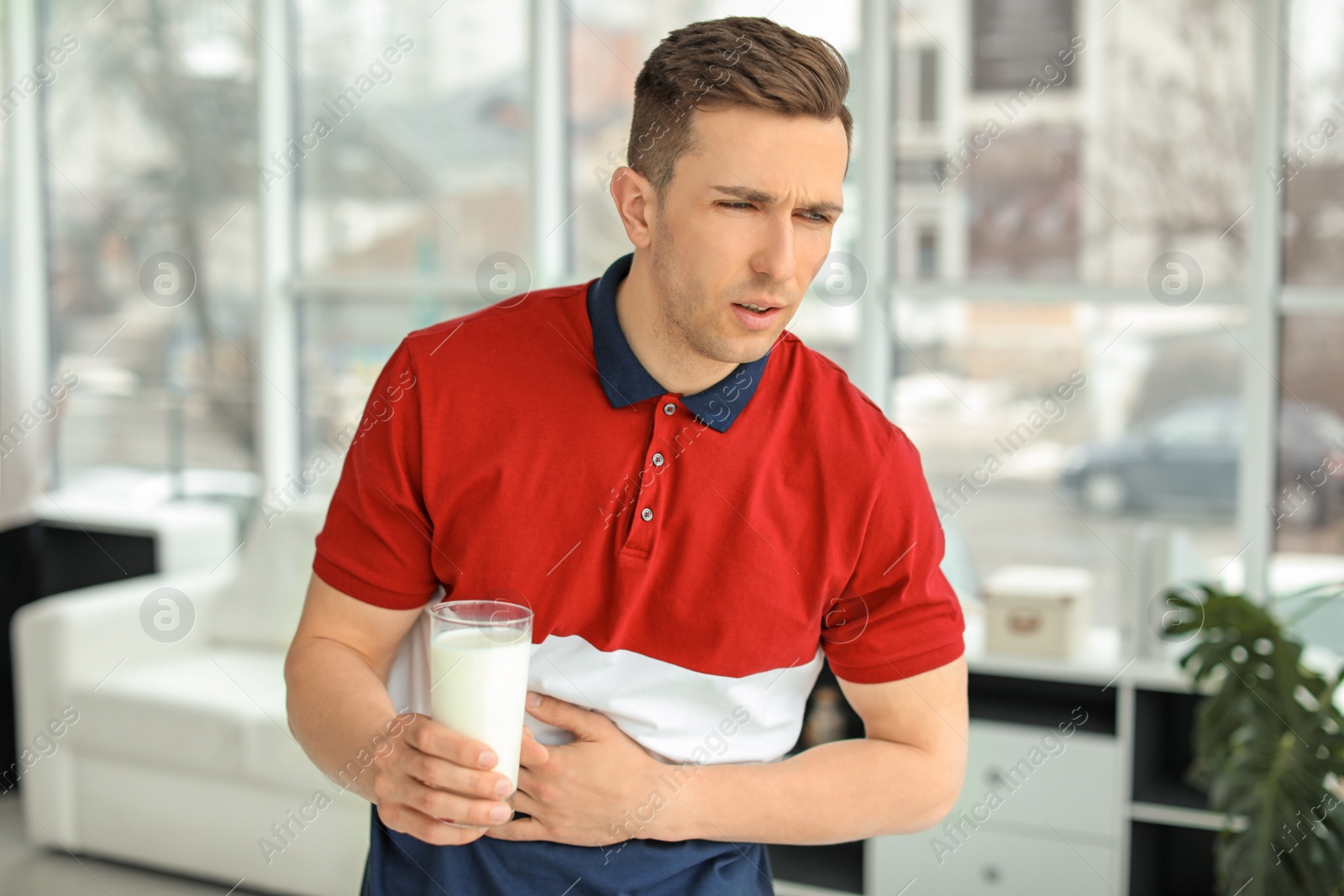 Photo of Young man with dairy allergy holding glass of milk indoors