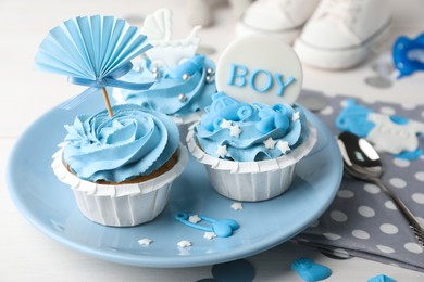 Photo of Delicious cupcakes with light blue cream and toppers for baby shower on table