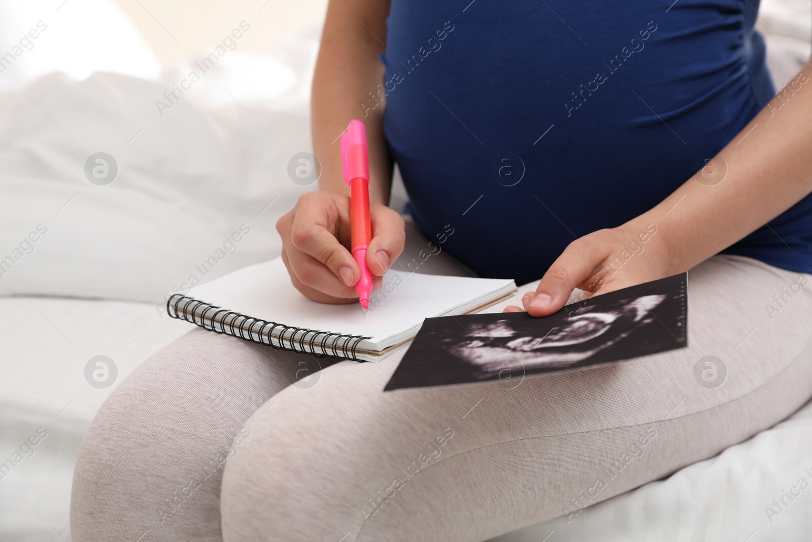 Photo of Pregnant woman with notebook and sonogram choosing name for baby on bed, closeup