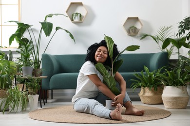 Photo of Relaxing atmosphere. Happy woman hugging ficus around another potted houseplants in room