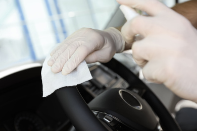 Photo of Man cleaning steering wheel with wet wipe and antibacterial spray in car, closeup