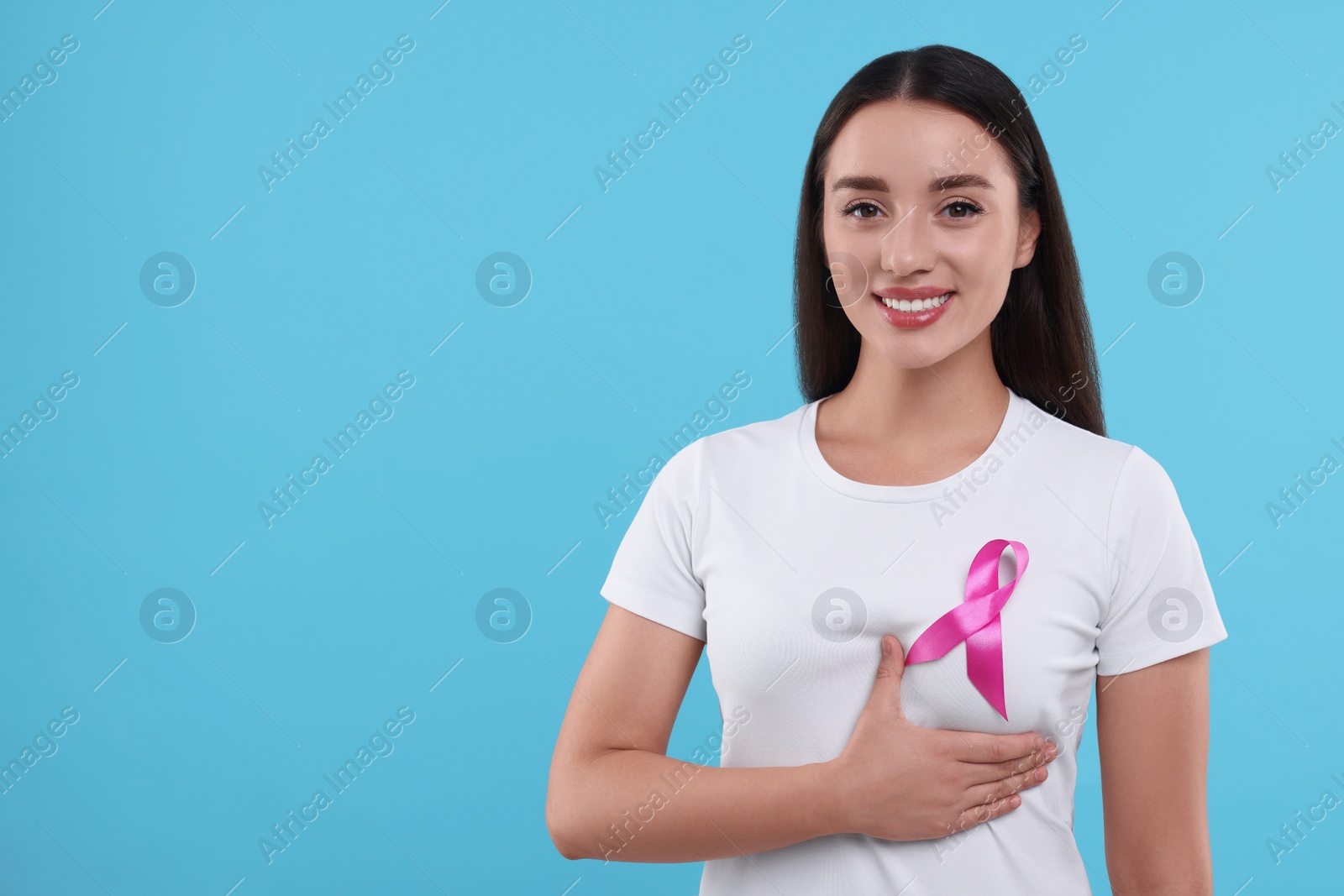 Photo of Beautiful happy woman with pink ribbon on light blue background, space for text. Breast cancer awareness