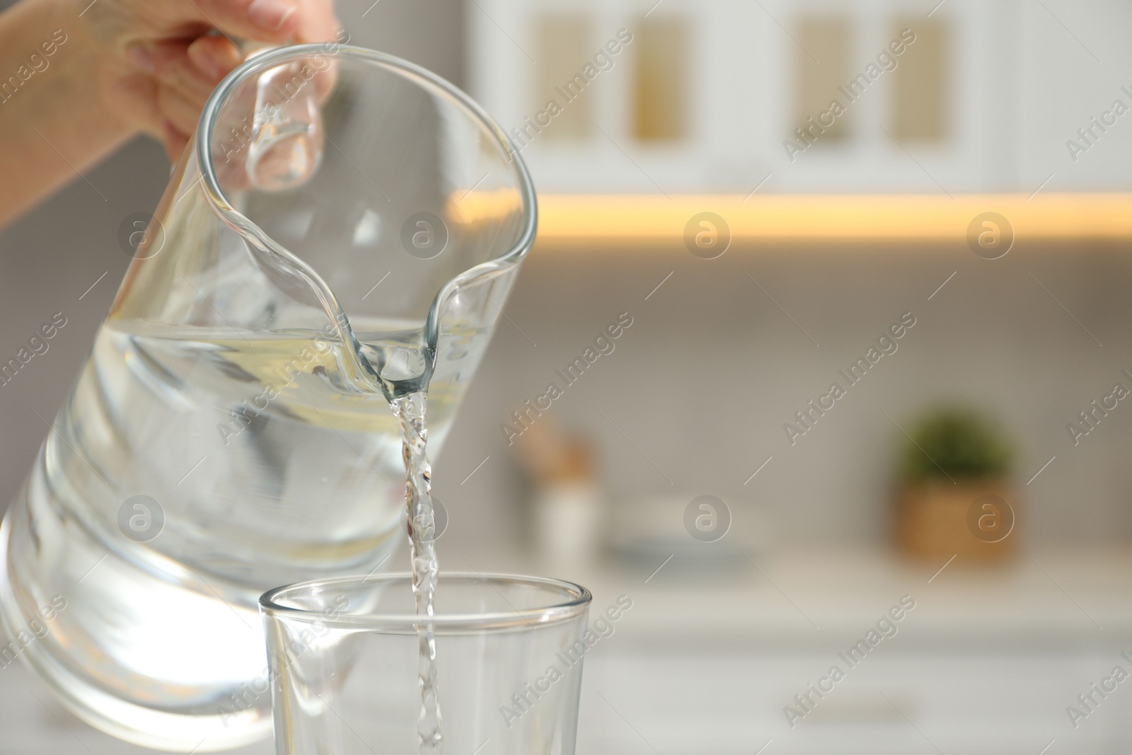 Photo of Woman pouring water from jug into glass in kitchen, closeup. Space for text
