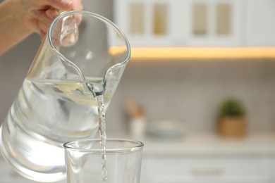 Photo of Woman pouring water from jug into glass in kitchen, closeup. Space for text