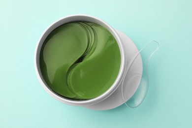 Photo of Jar of under eye patches and spoon on turquoise background, top view. Cosmetic product